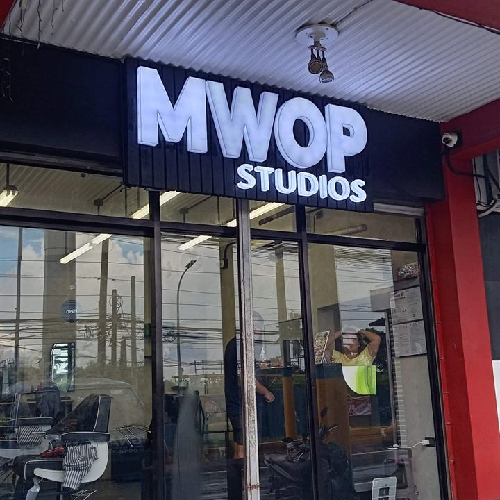 White back-lit acrylic letters spelling MWOP Studios above a glass storefront